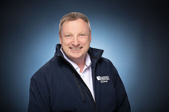 Das Bild zeigt ein Portrait von Herrn Volker Rozek - Auffällig ist die blaue Arbeitsjacke, welche im Brustbereich auf der linken Seite mit seinem Firmenlogo versehen ist.